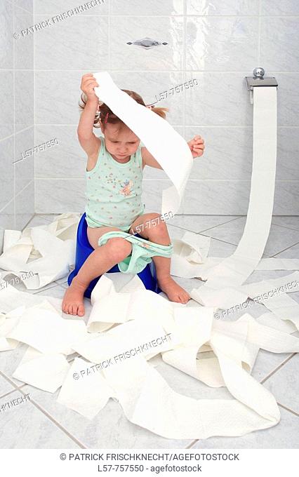 Little girl sitting on Potty in bathroom, unrolling toilette paper while doing potty training, playing and fooling around