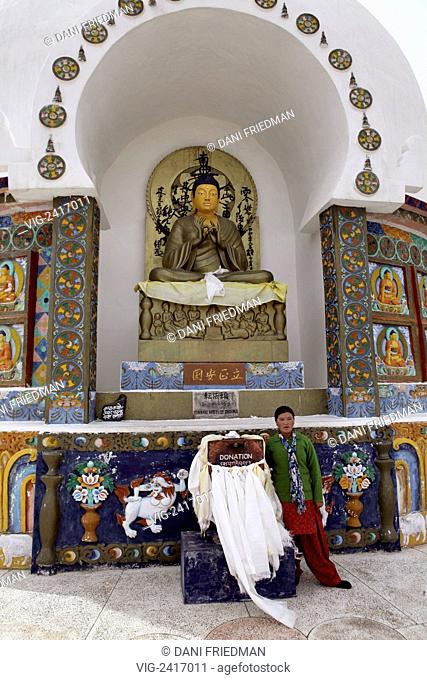 INDIA, CHANGSPA, 12.07.2010, A Ladakhi woman poses for a photo by a large statue of Lord Buddha depicting the turning the Wheel of Dharma in the Shanti Stupa in...