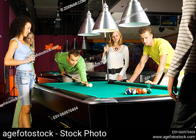 Large group of teenagers standing at pool table. Smiling and looking at balls. One person is playing billard