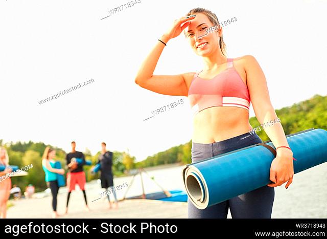 Sportliche junge Frau als Coach mit Yogamatte nach einem Fitness Kurs am Seeufer