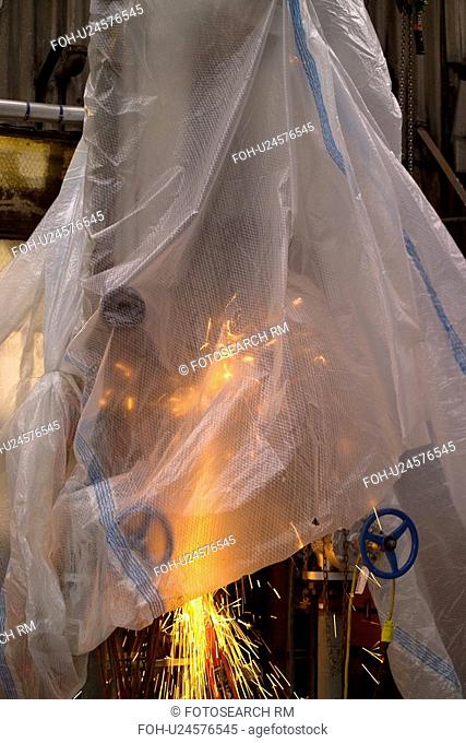 Oil Refinery Worker Grinding Pipe with Plastic Sheeting Cover