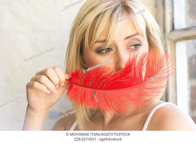 Young woman hiding face with a red feather