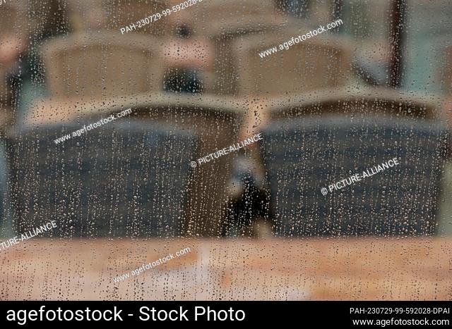 29 July 2023, Saxony-Anhalt, Wernigerode: Raindrops collect on a glass pane on the market square, in the background the exterior of a cafe