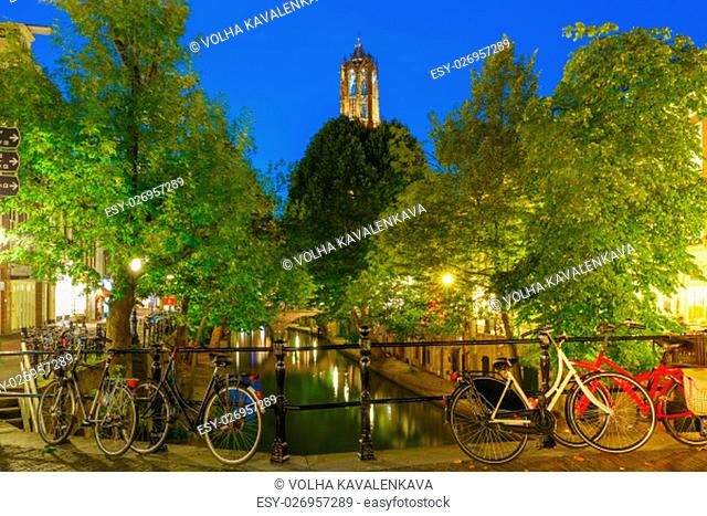 Dom Tower and bridge with bikes over canal Oudegracht in the night colorful illuminations in the blue hour, Utrecht, Netherlands