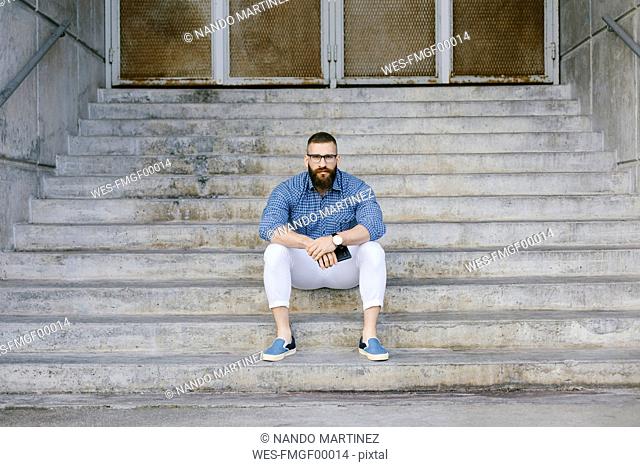 Portrait of bearded hipster businessman with smartphone sitting on stairs
