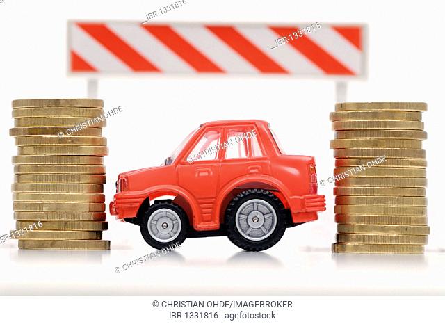 Miniature car between stacks of coins, symbolic image for car tolls and taxes