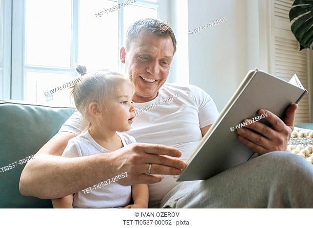 Father reading book to daughter on sofa