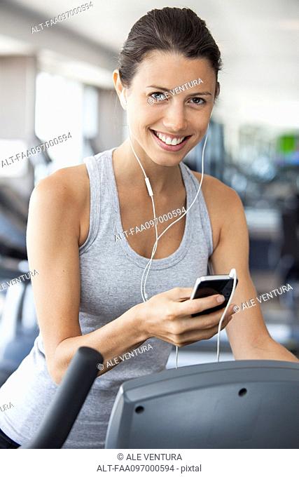 Young woman listening to music while using step climber at gym