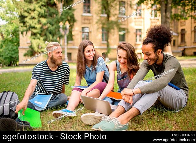 University students studying on grass. Young people sitting on lawn laughing and working on hometasks