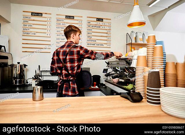 young barista wearing aprons using a coffee machine to make coffee in cafe