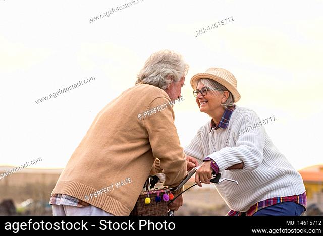 two seniors together smiling and enjoying looking each other - mature woman with a bike looking at the pensioner man with love