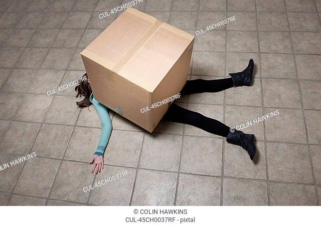 Teenage girl lying under cardboard box