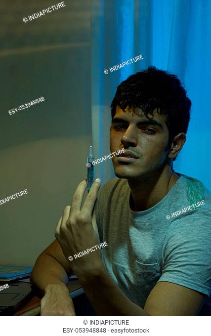 Portrait of male drug addict holding syringe at home