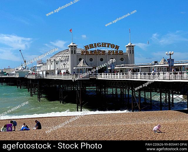 26 June 2022, Great Britain, Brighton: Guests sitting in front of Brighton Pier on the beach. Photo: Benedikt von Imhoff/dpa