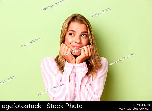 Close-up of beautiful blond girl dreaming about something, leaning on hands and smiling, looking left, standing over green background