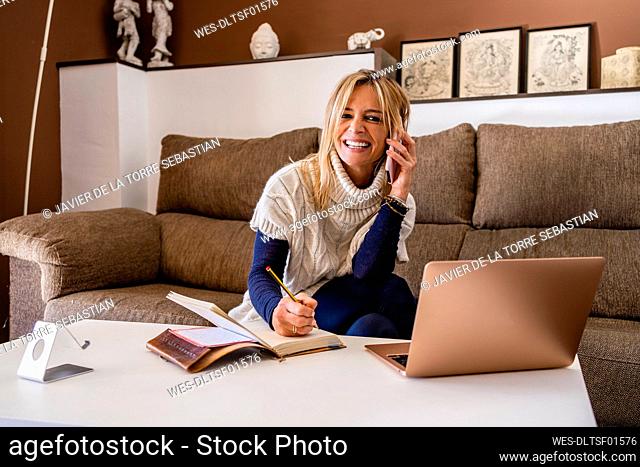 Smiling psychologist with book and pen talking on phone call while working in office