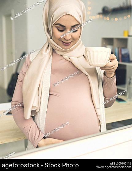 Pregnant woman with coffee cup seen through window