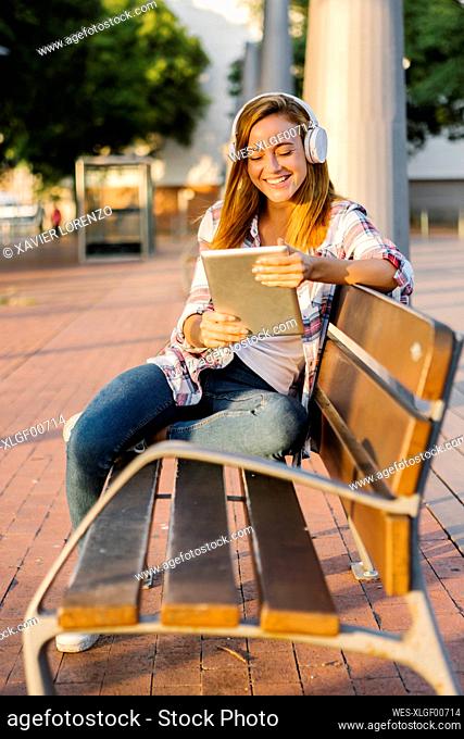 Smiling woman using digital tablet while sitting on bench during sunny day