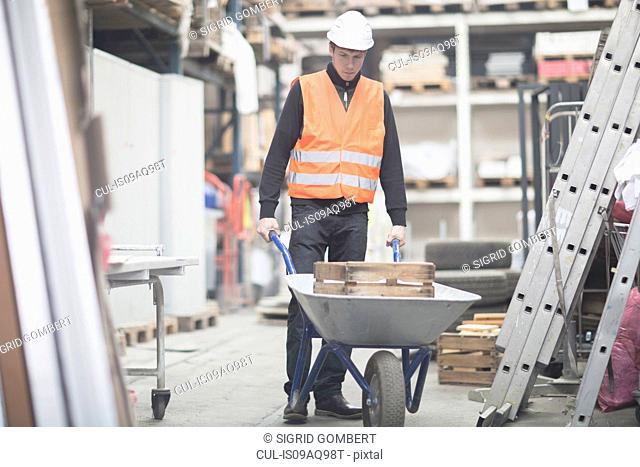Young male warehouse worker pushing wheelbarrow in warehouse