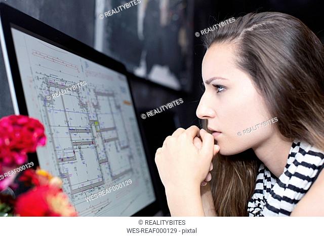 Young woman looking at construction plan on computer monitor
