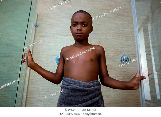 Low angle portrait of shirtless boy wrapped in towel standing amidst glass