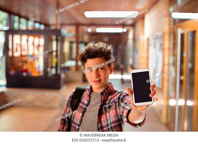 Schoolboy standing with schoolbag showing mobile phone in corridor at school