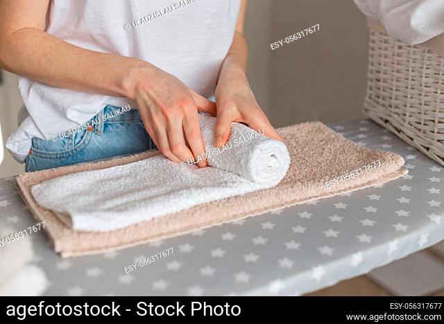 Woman rolling ironed clean towels standing at ironing board. Laundry service or cleaning housework concept