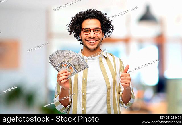 happy man with money showing thumbs up at office