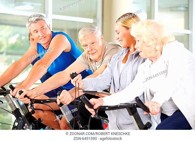 Trainerin mit Stoppuhr zwischen Senioren beim Spinning im Fitnesscenter