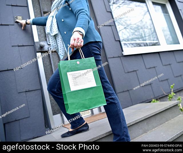 02 April 2020, North Rhine-Westphalia, Gelsenkirchen: A woman hands out a bag for home to a parishioner. The catholic parish of Hippolytus offers a bag for the...