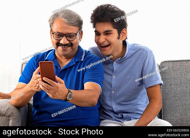 Indian father and son sitting on sofa and enjoying with mobile