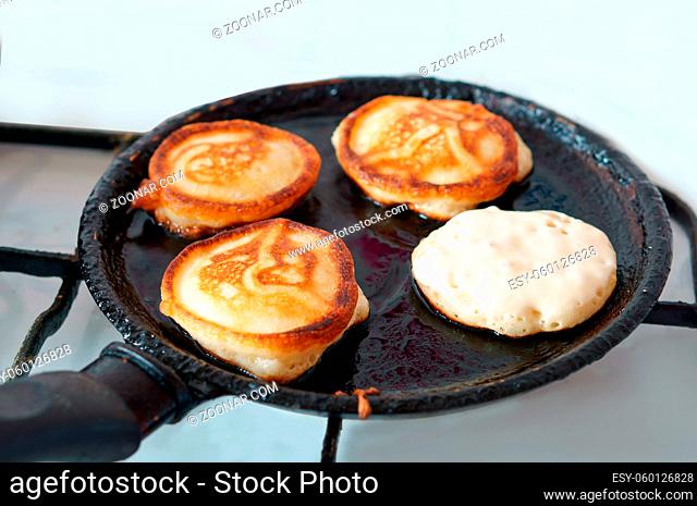 four pancakes are cooked in oil on a frying pan, pancakes are fried in a frying pan