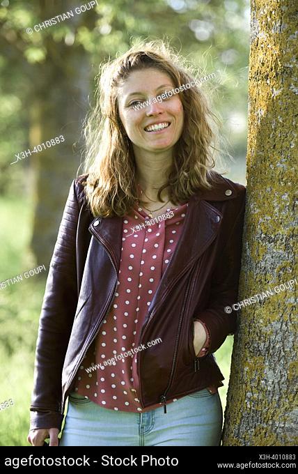 Jeune femme portant un blouson de cuir, adossee au tronc d'un arbre. Departement d'Eure-et-Loir, region Centre-Val-de-Loire, France