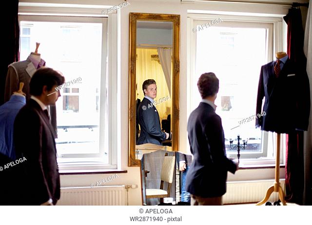 Fashion designer looking at male customer wearing suit in boutique