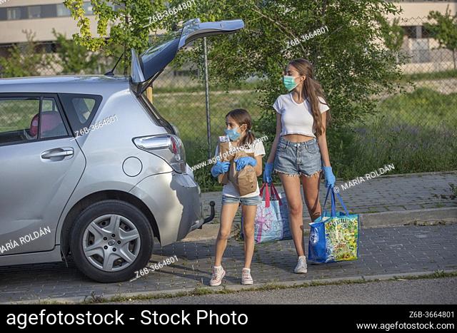 sisters wearing masks and gloves ready to cross the street with groceries bags