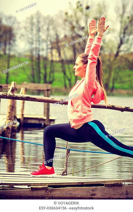 Sports and activities concept. Slim fit attractive woman exercising stretching outdoor. Young motivated girl training in sporty clothes on lake shore