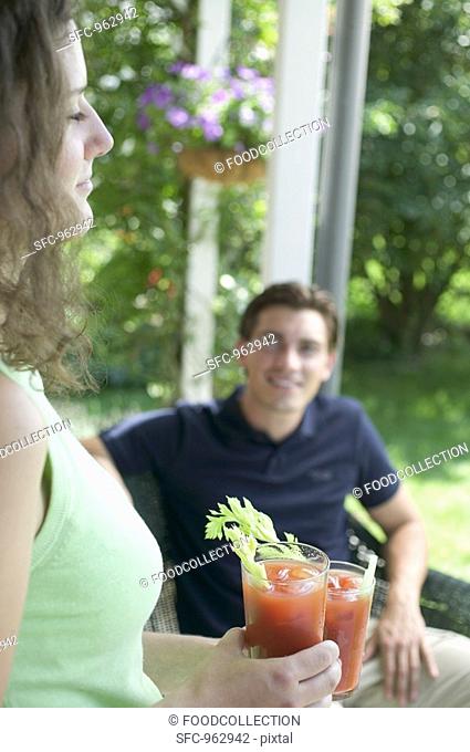 Young woman with two tomato drinks, man in background