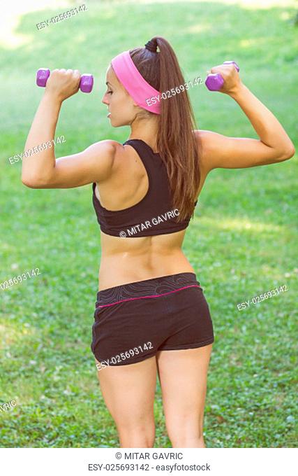 Fitness Slim Woman Training with dumbbells. Female practicing using hand weights outdoor. Healthy lifestyle workout concept on beautiful summer day