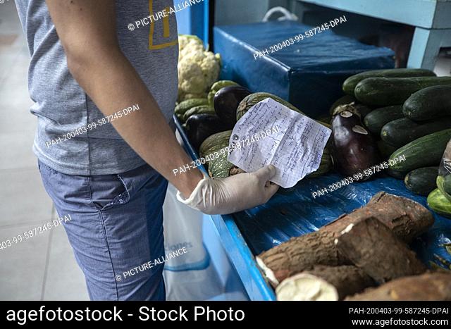 03 April 2020, Peru, Lima: A man wearing latex gloves against the spread of the coronavirus holds a shopping list at a vegetable stand in a market