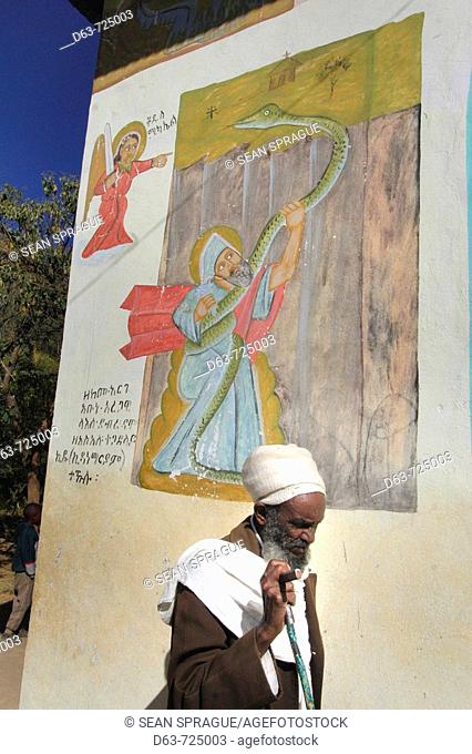 Priest walking passed mural depicting Abuna Aregawi and the serpent, Kidana Merhet church, Tigray, Ethiopia