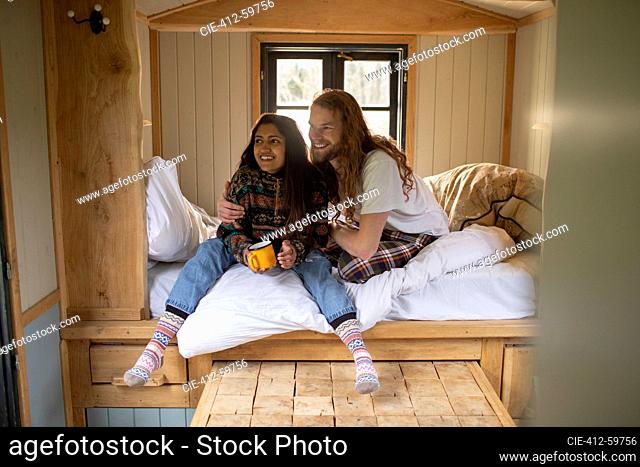 Happy young couple relaxing with coffee in tiny cabin rental bed