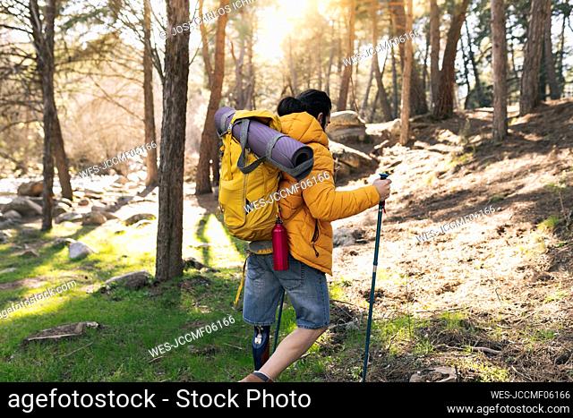 Disabled man wearing backpack walking with hiking poles trekking in forest
