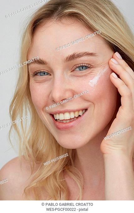 Portrait of smiling young woman applying cream on her face