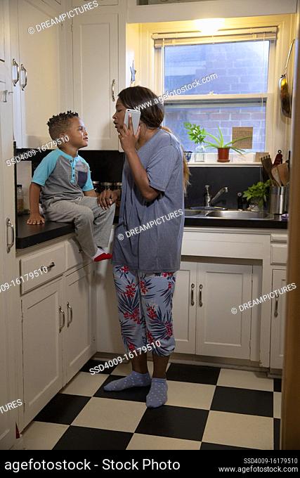 Mom at home in kitchen with son sitting on counter while talking to doctors on the phone