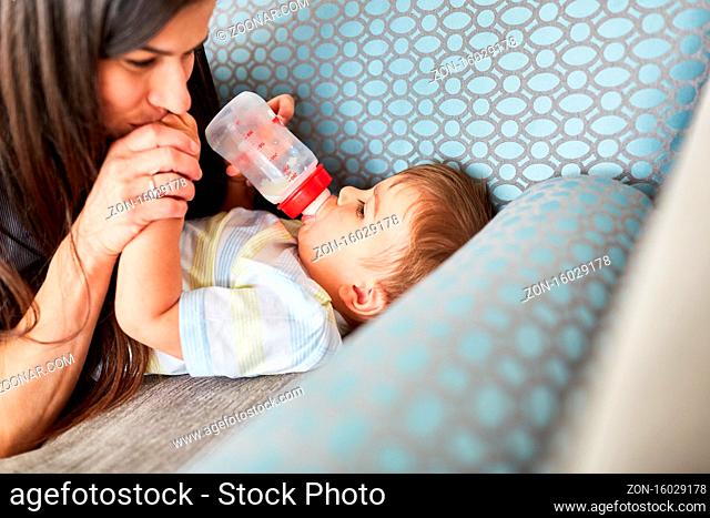 Mutter gibt Baby die Flasche Milch auf dem Sofa als Konzept für Liebe und Fürsorge