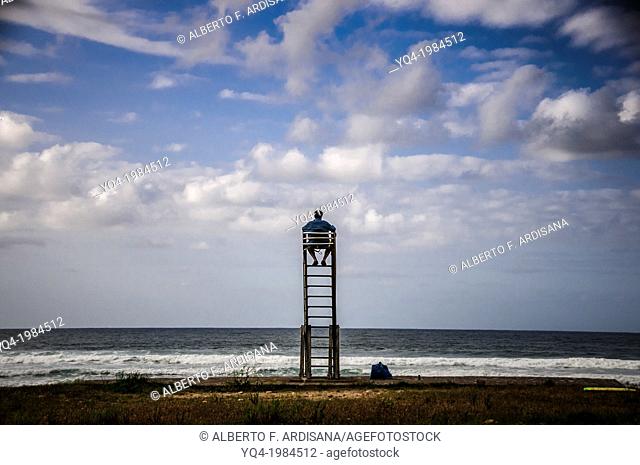 A man watches the skyline from a lifeguard chair, Caravia, Asturias