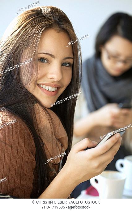 Beautiful young girl smiling in front of the camera while holding a smartphone