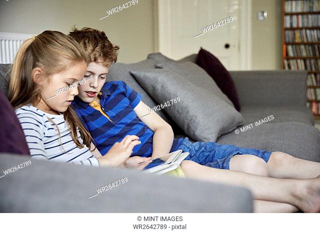 Two children seated sharing a digital tablet watching the screen