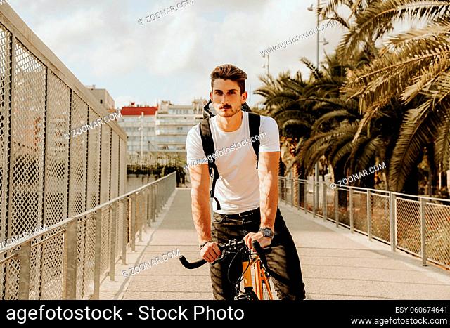 The young man in casual clothes is cycling on the road in the evening city. High quality photo
