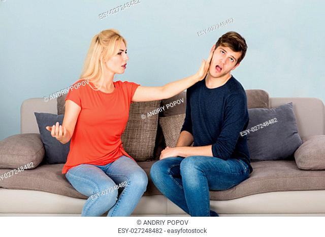 Angry Woman On Couch Slapping Her Husband While Quarreling About Infidelity And Divorce At Home